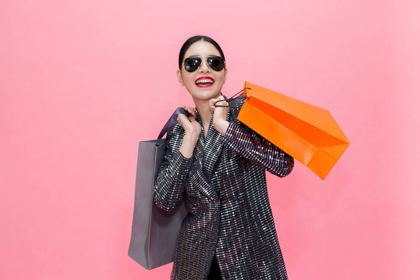 Young Stylish Asian woman carrying shopping bags and holding credit card. Beautiful fashionable woman with sunglasses isolated over pink background. Shopping and Finance concept - Fotografie, Obrázek