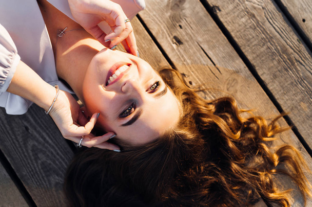 a sincere smile of a girl who lying on a wooden surface and the sunlight shining on her - Фото, изображение