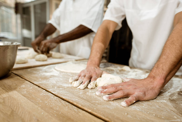 cropped shot of bakers kneading dough together at baking manufacture - Photo, Image