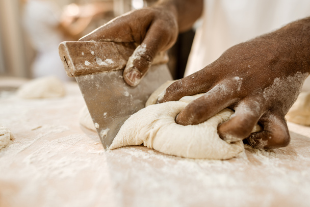 cropped shot of baker cutting raw dough with dough knife - Photo, Image