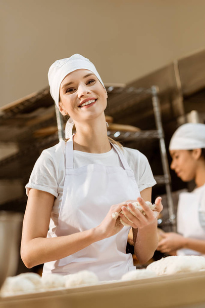 背景にぼやけている彼女の同僚と作業しながら製造をパンに練り女性の幸せのパン - 写真・画像