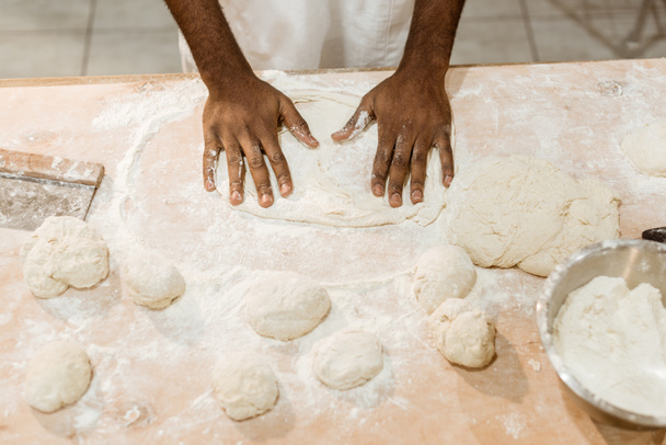 cropped shot of african american baker kneading dough for pastry on messy table - Photo, image