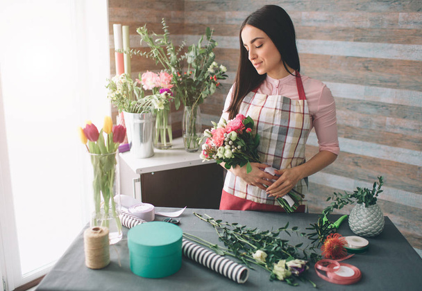 Female florist at work: pretty young dark-haired woman making fashion modern bouquet of different flowers. Women working with flowers in workshop - Photo, image