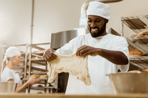 onnellinen komea afrikkalainen amerikkalainen leipuri valmistelee taikinaa leivontaan valmistus
 - Valokuva, kuva