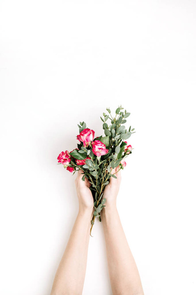 Las manos de la mujer sostienen flores de rosas y ramos de ramas de eucalipto sobre fondo blanco. Plancha plana, vista superior de fondo de primavera
. - Foto, Imagen