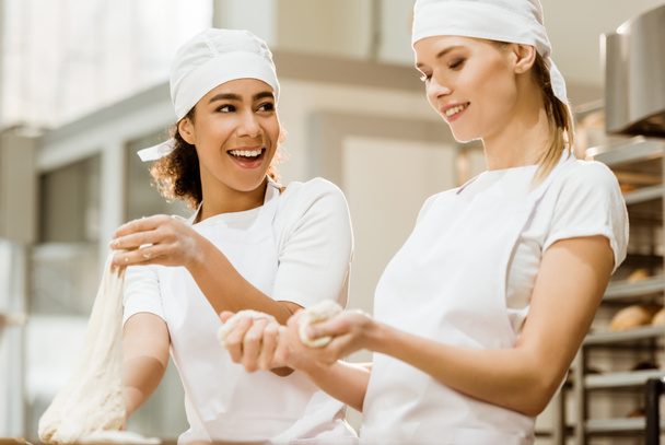Gelukkig vrouwelijke bakkers kneden van deeg samen bij het bakken van vervaardiging - Foto, afbeelding