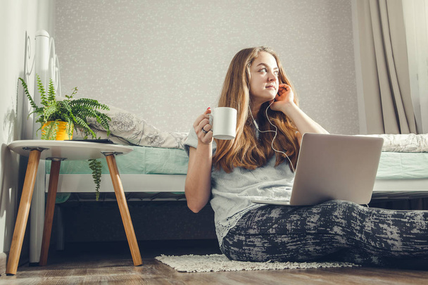Νεαρή γυναίκα που πίνει καφέ χρησιμοποιώντας το laptop στην κρεβατοκάμαρα και να ακούτε τη μουσική - Φωτογραφία, εικόνα