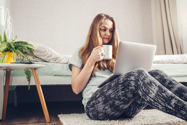 Mujer joven bebiendo café usando su portátil en el dormitorio
 - Foto, Imagen