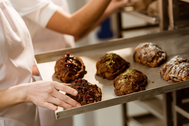 tiro recortado de panadero femenino sacando bandeja con pastelería dulce del horno
 - Foto, Imagen