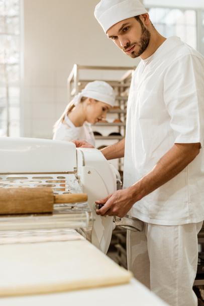 panadero guapo que trabaja con rodillo de masa industrial en la fabricación de la hornada
 - Foto, Imagen