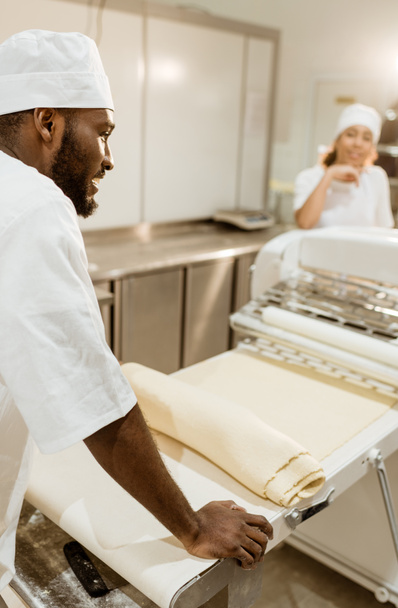 Afryki amerykański baker z rolki surowego ciasta podczas pieczenia produkcji - Zdjęcie, obraz