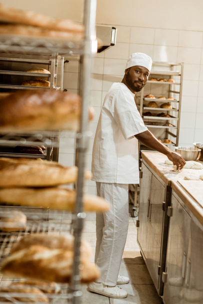 african american baker preparing raw dough at workplace on baking manufacture - Foto, afbeelding