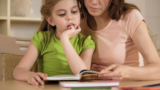 Madre de apoyo lectura libro de texto junto con hijita hiperactiva
 - Foto, Imagen