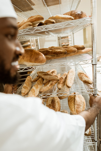 close-up shot of african american baker driving shelves of fresh bread on baking manufacture - Фото, изображение