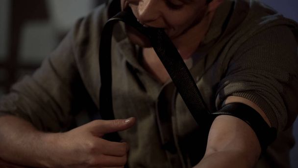 Mužské feťák drží škrtidlo s jeho zuby, příprava léků injekce - Fotografie, Obrázek