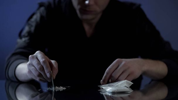 Young wealthy man forms cocaine lines on table, drug addiction among the rich - Foto, immagini