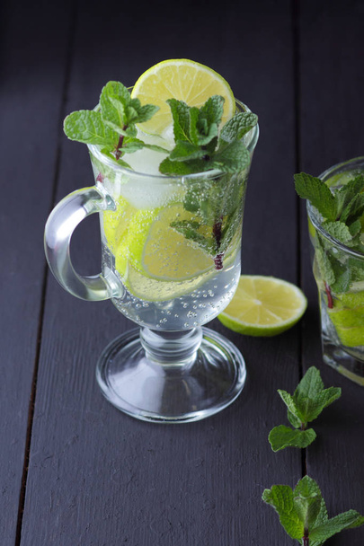 Mojito on a dark background, summer cocktail with lime and mint, refreshing drink with lemon, fresh mint for cocktail, minimalist cocktail, celebratory drink with ice, vegan, copy space, blank for designer - Foto, Bild