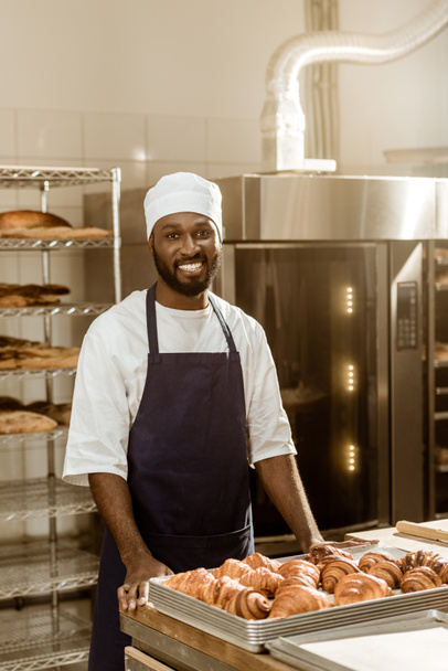 Porträt eines gut aussehenden afrikanisch-amerikanischen Bäckers am Arbeitsplatz bei der Backmanufaktur - Foto, Bild