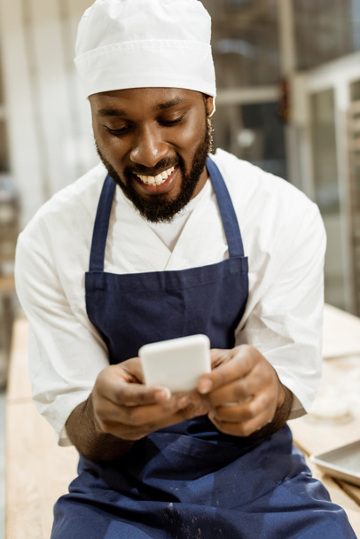 young african american baker with hands covered in flour using smartphone - Valokuva, kuva