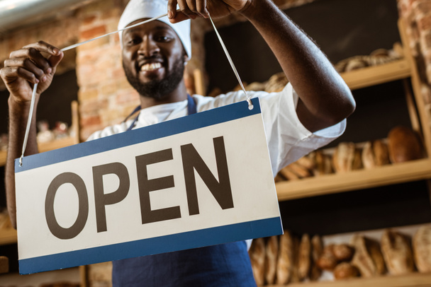 happy african american baker holding open sign at pastry store - Photo, Image