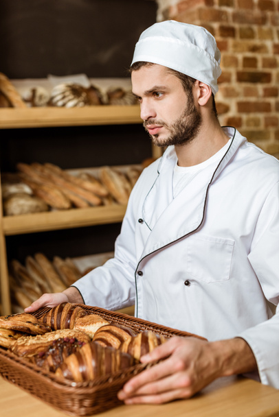 handsome baker holding tray with croissants at pastry store - Foto, afbeelding