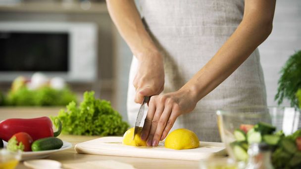 Female chef cutting lemon with sharp knife for lunch preparing, cooking tips - Φωτογραφία, εικόνα