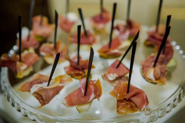 ham snacks on black skewers served on glass plateau in catering service - Foto, Bild