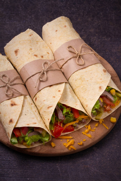 Wraps with beef, tomatoes, lettuce, cucumbers, cheese and sweet corn on cutting board. Tortilla, burritos, sandwiches twisted rolls.  - Foto, immagini