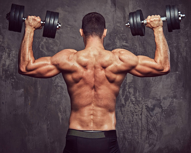 Brutální sportovní vousatých shirtless muž dělá cvičení. Na šedém pozadí, samostatný. - Fotografie, Obrázek