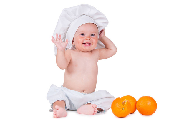 A small child eats an orange slice in a chef suit on a white background. - Foto, imagen