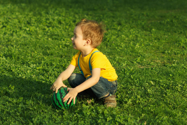 Cute positive kid, playing happily with ball on green meadow - Zdjęcie, obraz