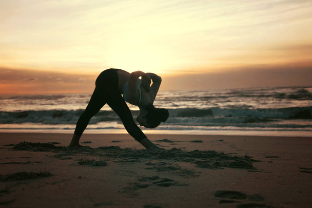 Urheilullinen nuori nainen joogaharjoituksissa rannalla
 - Valokuva, kuva