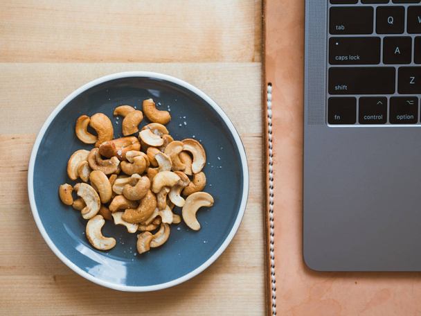 Some cashew nuts on small snack dish on work desk. - Fotó, kép