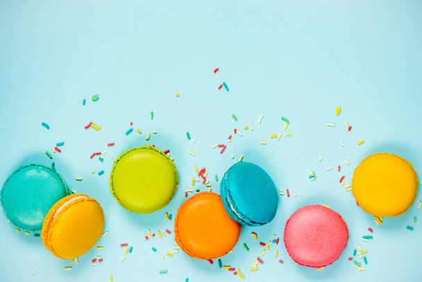 Top view of colorful macaroons and sugar sprinkles arranged over blue background.  - Photo, image