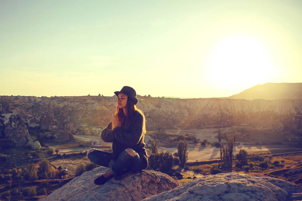 Joven chica hermosa practicando yoga en la cima de una montaña en Capadocia al amanecer. Prácticas de relajación
. - Foto, Imagen