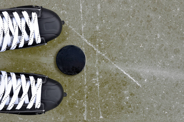 Pair of hockey skates with puck on a ice rink. - Fotó, kép