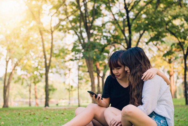 Dwóch przyjaciół piękny szczęśliwy młodych Azjatek, wspólna zabawa w parku i biorąc selfie. Szczęśliwy hipster młode Azjatki uśmiechając się i patrząc na smartfonie. Pojęcia dotyczące stylu życia i przyjaźni. - Zdjęcie, obraz