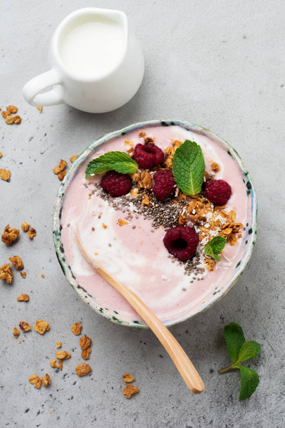 Pink raspberry banana smoothie bowl with granola, chia seeds, coconut and mint on light gray concrete background. Selective focus. Top view. Copy space. - Zdjęcie, obraz