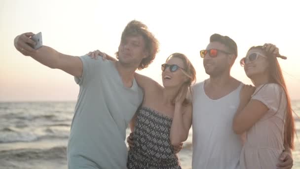Ritratto di quattro persone con bianchi sorrisi dentati che scattano selfie dal telefono cellulare Trascorrere del tempo insieme sulla spiaggia durante il tempo ventoso
. - Filmati, video