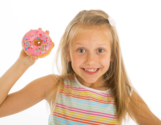 young beautiful happy and excited blond girl 8 or 9 years old holding donut desert on her hand looking spastic and cheerful in sugar abuse and addiction - Photo, Image