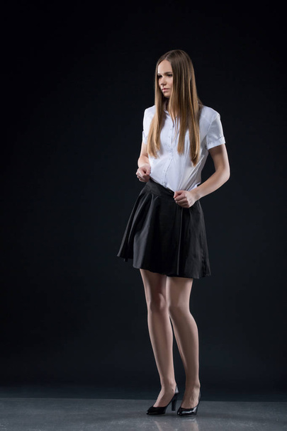 retrato de menina adolescente no fundo preto posando em uma blusa branca e saia preta curta, olhar de escritório. Estudante feliz ou estudante com cabelos longos olhando para a câmera no fundo preto
. - Foto, Imagem