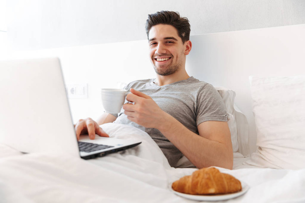 Photo of happy man in casual clothes having breakfast, while lyi - Photo, Image