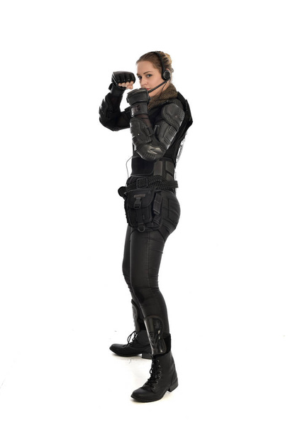 Pełna długość Portret żołnierz Kobieta w czarnej zbroi taktyczne, stojąc w profilu, na białym tle na tle białego studia. - Zdjęcie, obraz
