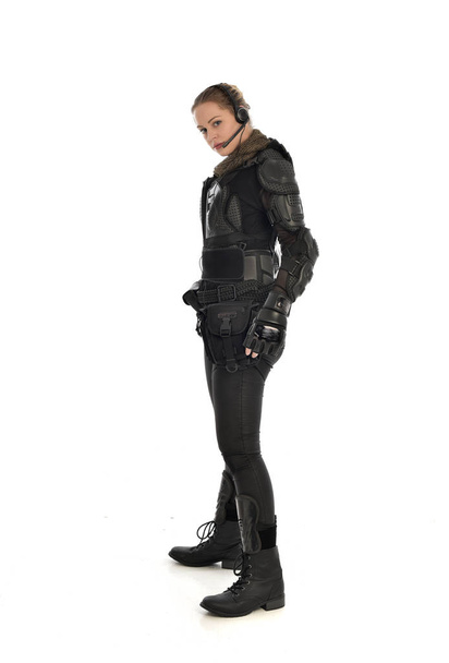 портрет женщины-солдата в черных тактических доспехах, стоящей в профиль, изолированной на белом фоне студии
. - Фото, изображение