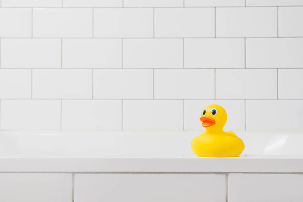 Speelgoed gele eend in de badkamer op een lichte baksteen-achtergrond - Foto, afbeelding
