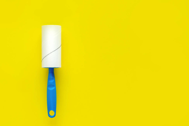 Limpador de roupas de rolo com fita adesiva e alça azul em um fundo amarelo. Plano de fundo leigo
. - Foto, Imagem