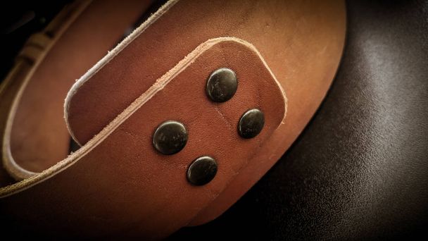 Un bellissimo cinturino in fionda marrone realizzato a mano in pelle su uno sfondo nero. Attrezzatura da fotografo, elegante, vintage, retrò
. - Foto, immagini