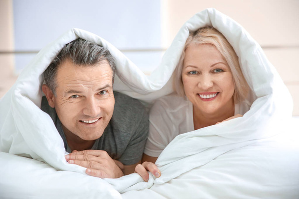 Senior couple under blanket in bed together at home - 写真・画像