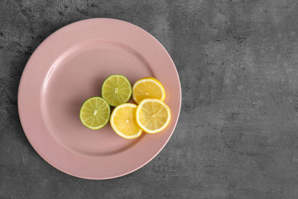 Plate with cutting lemon and lime on grey background - Фото, изображение