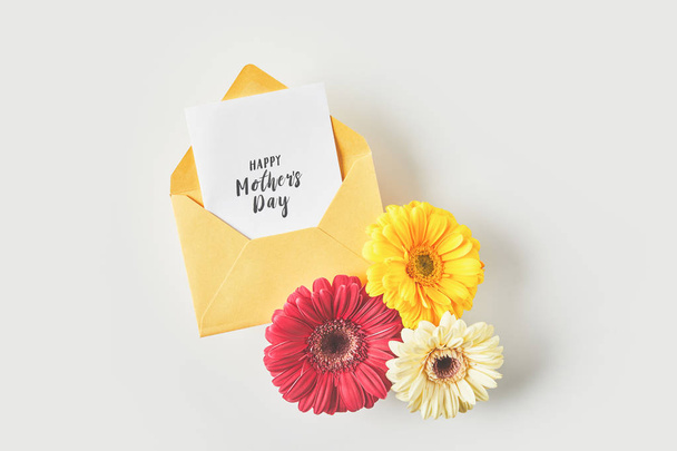 top view of happy mothers day greeting card in envelope and beautiful gerbera flowers on grey  - Фото, зображення